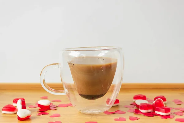 Glass double bottom cup of coffee on the wooden table with red paper hearts and candies. High quality photo