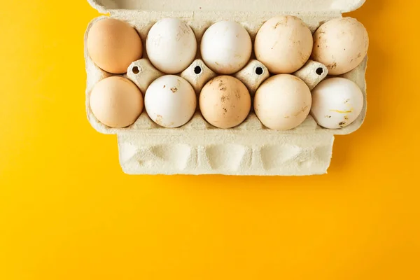Top view of open egg box with ten brown and white eggs isolated on yellow background. Fresh organic chicken eggs in carton pack. Easter holiday concept.