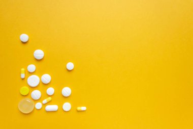 Pattern of different pills and capsules in the lower left corner. Isolated on yellow background. Healthcare and wellbeing concept. Space for text. Top view. Horizontal photo.