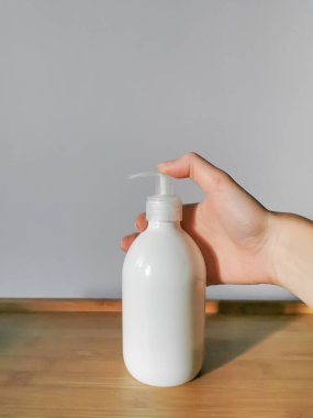 Woman's hand applying body lotion in white dispensser bottle on the wooden table. Demonstration of how to squeeze out body lotion. White background. Daily skin care concept.