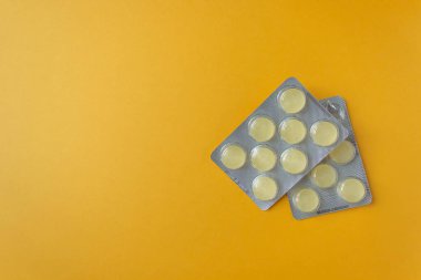 Two whole silver blister packs of yellow round cough drops. Yellow background and space for text. For sore throats and dry cough. Top view.