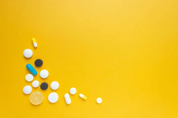 Group of multicolored pills and capsules in the lower left corner. Yellow background. Healthcare and longevity concept. Space for text. Horizontal flat lay composition.