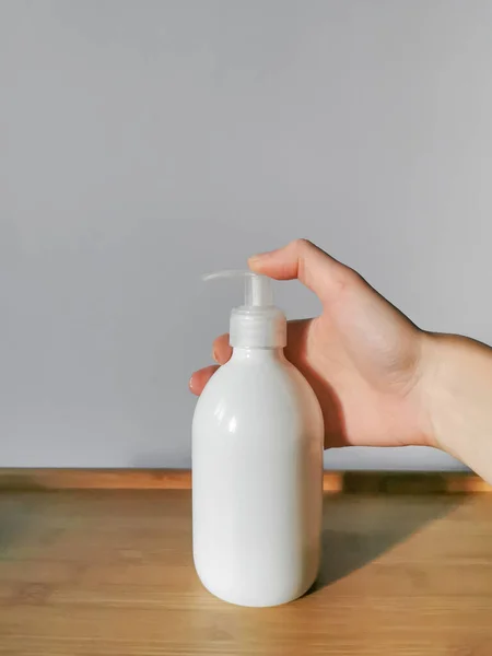Woman\'s hand applying body lotion in white dispensser bottle on the wooden table. Demonstration of how to squeeze out body lotion. White background. Daily skin care concept.