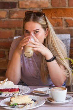 Kol saati olan genç bir kadın kafeteryada sabah kahvesi içerken raspberrie peynirli kek yiyor. Sarışın kadın kalori sayıyor ve sağlığına dikkat ediyor. Elinde bir bardak kahve tutarak ve eğlenerek..