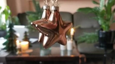 Hang and rotate two bronze, glass toys for decorating the Chistmas tree in the shape of stars. Blurred background. Preparation to decorate home for Christmas holidays concept.