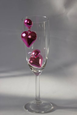 Pair of pink heart shaped earrings on the champagne glass isolated on white background. Romantic jewelry for Valentines party. Advertising still life product concept for Valentines Day. Holidays sale.