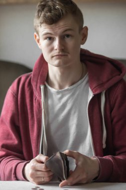 Sad young bankrupt showing his empty wallet and looking at camera. Upset man feeling stressed while looking at his billfold without money. Bankruptcy, poverty and unemployment concept. High inflation.