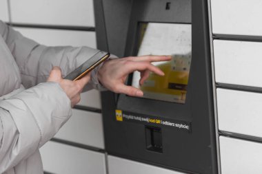 Pniewy, Poland - 22 January 2023. Man with smartphone entering code to open shopping locker in inPost delivery service. E-commerce shipping and delivery. People and gadgets concept.