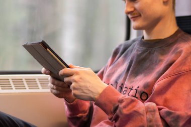 Smiling young man reading e-book when he traveling by train. Man sits at the train window and using digital tablet, watching movie, using mobile app, browsing internet, social media, shopping online.
