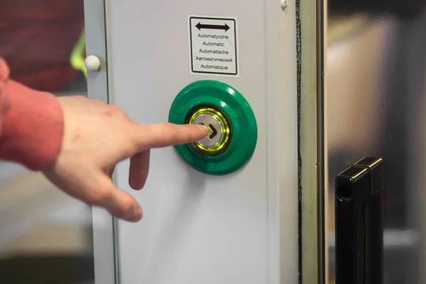 Mans hand index finger presses the door control green button to open automatic doors in a modern electric train or subway car, close-up. Responsible passenger. Public transport regulations concept.