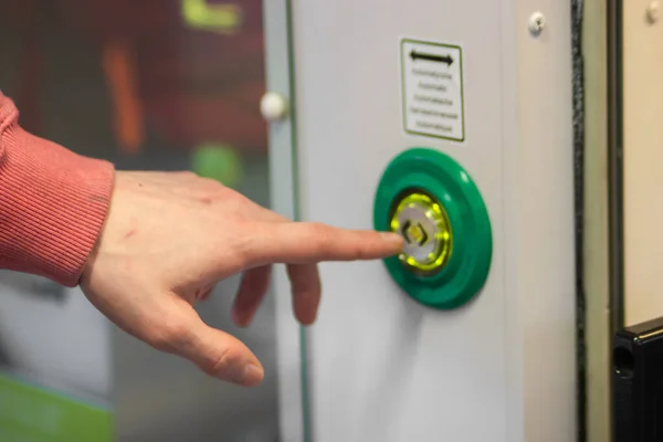 Mans hand index finger presses the door control green button to open automatic doors in a modern electric train or subway car, close-up. Responsible passenger. Public transport regulations concept.