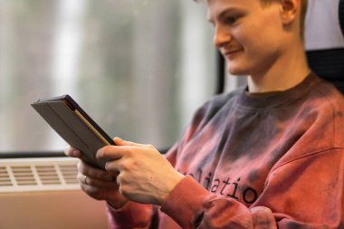 Smiling young man reading e-book when he traveling by train. Man sits at the train window and using digital tablet, watching movie, using mobile app, browsing internet, social media, shopping online.