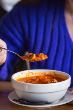 Mavi kazaklı genç bir kadın lezzetli domates çorbası, gazpacho ya da kızarmış ekmek, sebze ve sebze çorbası yiyor. Kadınların eli bir kase kırmızı çorbanın üstünde dolu bir kaşık tutar. Yemek molası konsepti.