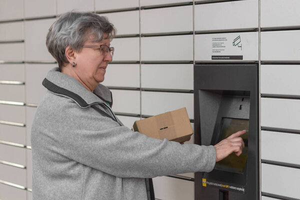 Pniewy, Poland - 22 March 2023. Shopping locker inPost with senior womans hand entering code to open it and send a parcel box. E-commerce shipping and delivery concept. Modern technology.