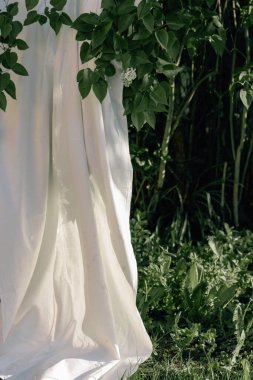 Beyaz çarşaf, yemyeşil yapraklı bir leylak dalında sallanıyor ve kuruyor. Bahar doğası. Boho stili kavramı. Kır evi çekirdeği ve kırsal estetik gün batımında. Metin için boşluk.