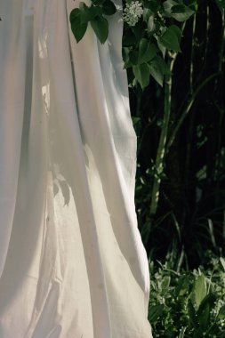 Beyaz çarşaf, yemyeşil yapraklı bir leylak dalında sallanıyor ve kuruyor. Bahar doğası. Boho stili kavramı. Kır evi çekirdeği ve kırsal estetik gün batımında. Metin için boşluk.