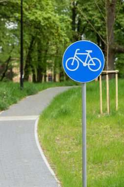 Mavi yuvarlak arka planda beyaz bisiklet şeridi trafik levhası. Metal bir direkte bisiklet tabelası, şehir parkında dar bir caddede bulanık bir sokak. Motosiklet dostu ve ekoloji taşımacılığı kavramı.