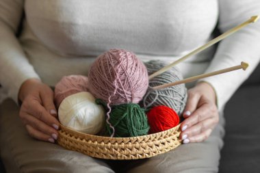 Yaşlı kadınların elleri, örgü örmek ve örgü örmek için pençe ve iplik kepçeleriyle dolu bir sepet tutuyor. Pembe, beyaz, kırmızı ve yeşil doğal yün toplar. Hobi, zanaat ve DIY konsepti.