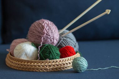 Mavi kanepede izole edilmiş sepetteki renkli iplik topları ve örgü iğneleri. Pembe, beyaz, kırmızı ve yeşil doğal yün pençeler. Kadın hobisi ve hala hayat konsepti. El işi ve arama..