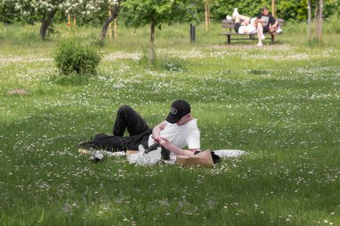 Şehir parkında battaniyenin üzerinde yatarken beyzbol şapkalı, cep telefonu kullanan beyaz bir genç. Yaz haftasonu piknikte fast food ile birlikte. Yeşil çimen.