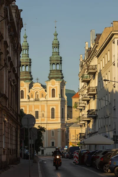 stock image Poznan, Poland - June 12, 2023: view of Dluga street with St. Francis Seraphim church during sunset, golden hour. Architecture in old town, two towers of famous church. The road traffic of a big city.