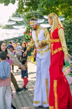 Almaty, Kazakistan - 18 Eylül 2022 'de Kazakistan' da bir adam ve ulusal Kazak kostümlü bir kız ayaklıklar üzerinde durup, parktaki tatilde kasaba halkını selamlıyorlar.