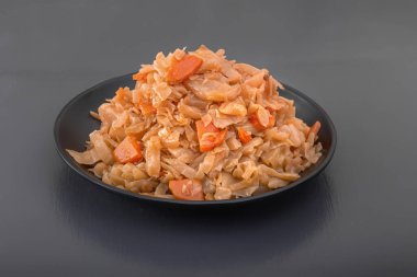 Stewed cabbage - bigos in a black plate on a dark background. Close-up