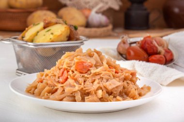 Stewed cabbage - bigos in a white porcelain plate against the background of pickled vegetables and baked potatoes. Close-up