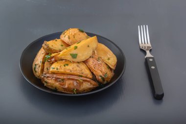 Baked potato wedges with herbs and salt in a black plate on a dark background. Close-up