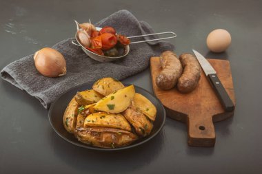 Izgara sosisli fırında patates dilimleri ve arka planda mayalanmış sebzeler..