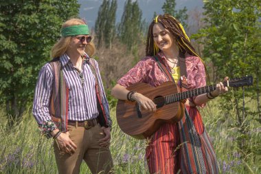 Güneşli bir günde ormanda gitarlı bir kızla hippi tarzı bir adam.