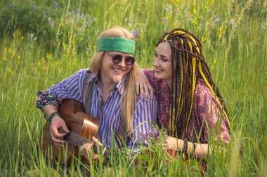 Adam ve gitarlı hippi tarzı bir kız güneşli bir günde ormanda çimlerin üzerinde oturuyorlar. Kapat.