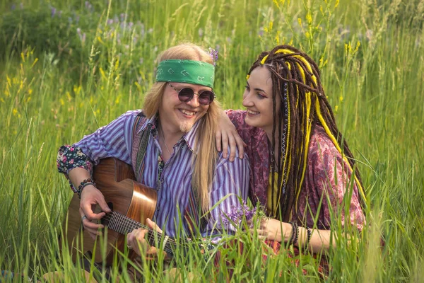 Guy and a girl in hippie style with a guitar are sitting in the grass on a forest glade on a sunny day. Close up