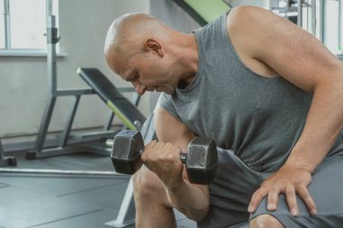 Spor salonunda pazı pompalamak için dambılla egzersiz yapan kaslı bir adam. Yakın plan.