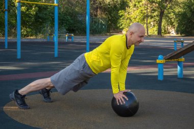 Avrupalı bir adam, sokak sporları sahasında bir tıp topuyla şınav çekiyor. Sağlıklı yaşam tarzı