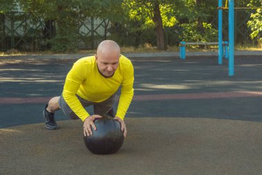 Avrupalı bir adam, sokak sporları sahasında bir tıp topuyla şınav çekiyor. Sağlıklı yaşam tarzı