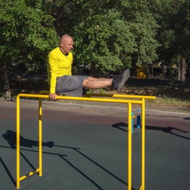 Adam güneşli bir yaz gününde sokak sporları alanında paralel barlarda egzersiz yapıyor. Sağlıklı yaşam tarzı