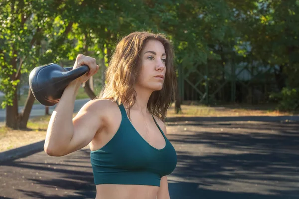 Genç bir kadın, güneşli bir günde bir sokak spor sahasında bir çaydanlıkla antrenman yapıyor. Sağlıklı bir yaşam tarzı. Yakın plan.