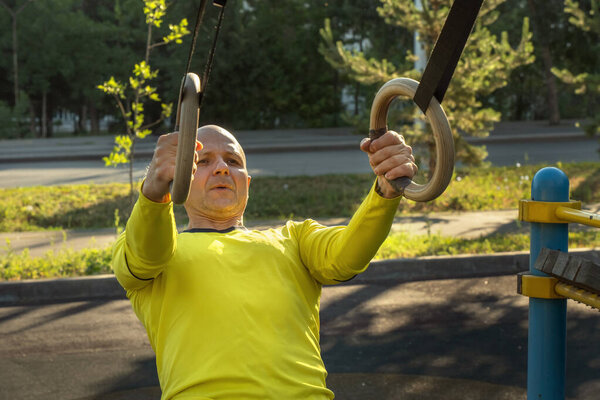 man trains with gymnastic rings on a street sports ground on a sunny day. Healthy lifestyle. Close-up