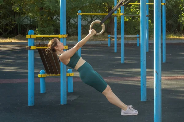 Çekici beyaz kadın spor sahasında spor yaparken jimnastik yüzükleriyle yanaşıyor. Sağlıklı yaşam tarzı