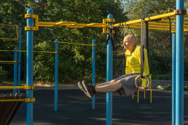 stock image Man performs a leg exercise on gymnastic rings on a street sports ground on a sunny day. Healthy lifestyle