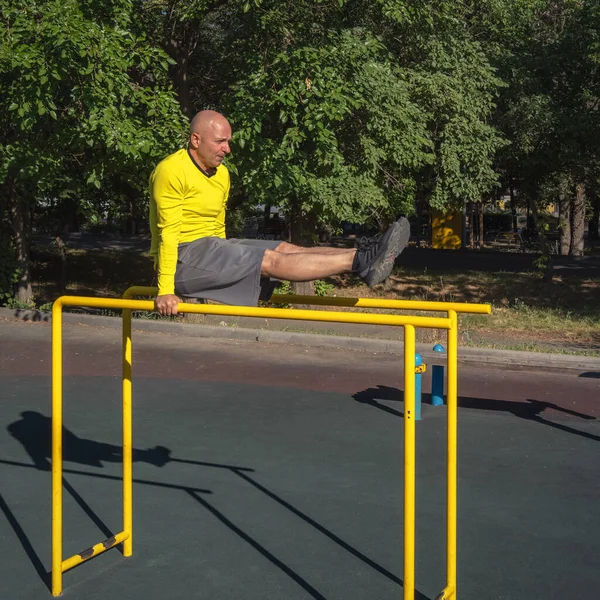 Adam güneşli bir yaz gününde sokak sporları alanında paralel barlarda egzersiz yapıyor. Sağlıklı yaşam tarzı