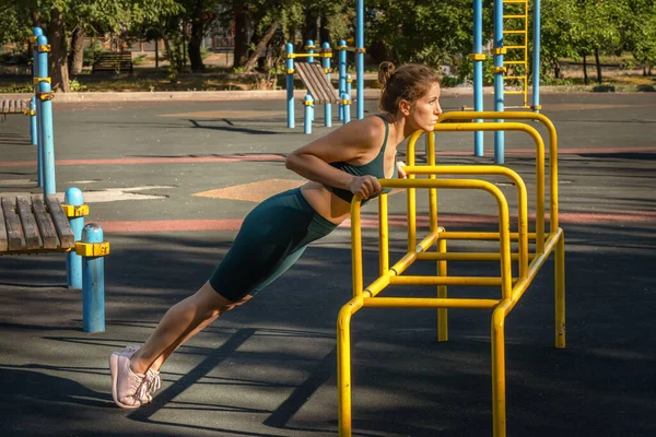 Genç Avrupalı bir kadın sokak spor sahasında metal simülatörde şınav çekiyor. Sağlıklı yaşam tarzı