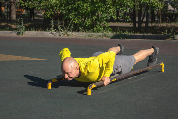 Man doing push-ups on parallel bars while exercising at an outdoor sports ground on a sunny summer day. Healthy lifestyle