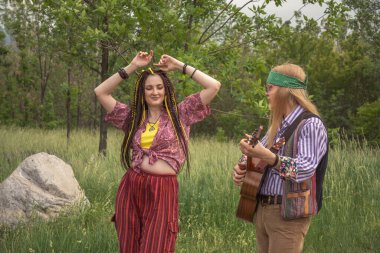 Hippi tarzı iki genç insan. Bir kız dans ediyor, bir erkek güneşli bir günde şehir yolunda gitar çalıyor.