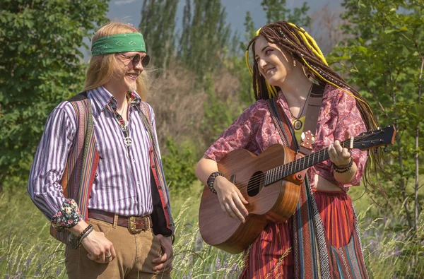 Guy and a girl in hippie style with a guitar in a forest clearing on a sunny day