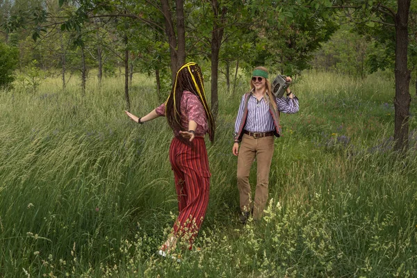 Couple of young people in a hippie style in the forest. A girl is dancing, a guy is carrying a cassette retro tape