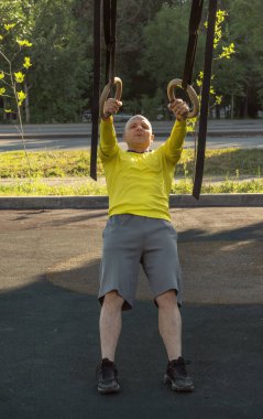 Adam güneşli bir günde sokak sporları sahasında jimnastik halkalarıyla egzersiz yapıyor. Sağlıklı yaşam tarzı