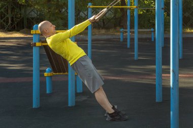 Adam güneşli bir günde sokak sporları sahasında jimnastik halkalarıyla egzersiz yapıyor. Sağlıklı yaşam tarzı