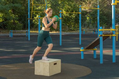 Elinde top olan genç bir kadın, ayaklarıyla sokak sporları sahasında tahta bir kutuya atlıyor. Sağlıklı yaşam tarzı